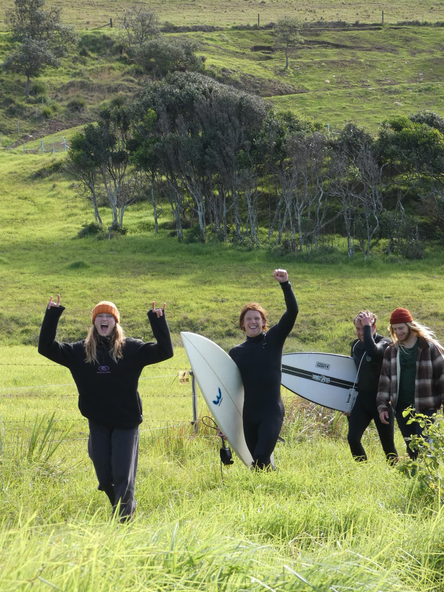 Crew walking out through a green field with surfboards, cheering